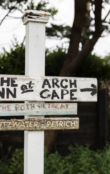 Rustic signpost directing to charming inn amid lush greenery and coastal retreat, promising serene getaway.