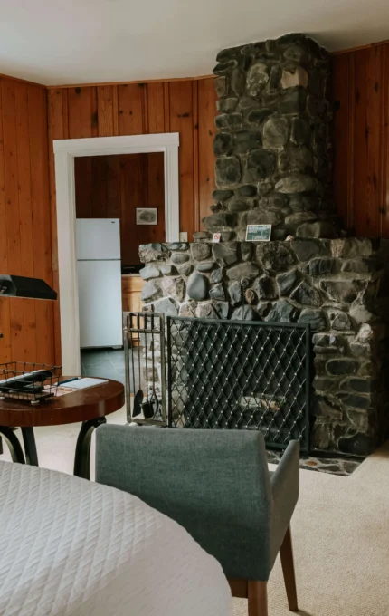 Homely hotel room with cosy stone fireplace, modern TV, wooden panelling, and sitting area. Ideal for relaxing stays.