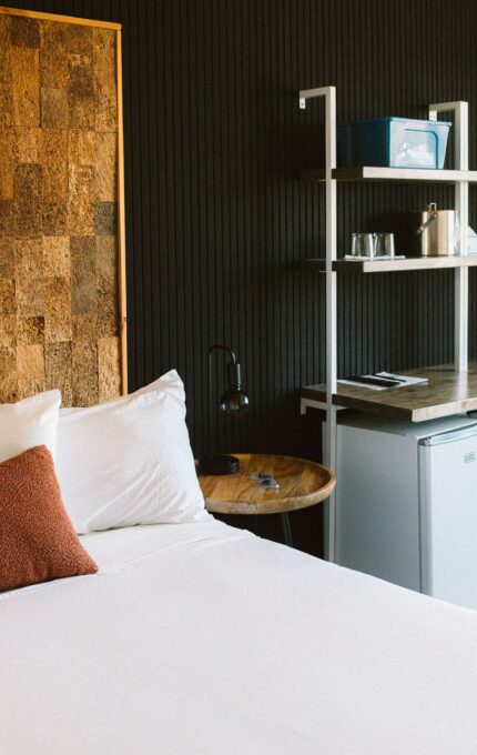 King room at the Adrift Hotel in Long Beach, Washington, with a cork accent headboard wall, work desk, and mini fridge by the window.