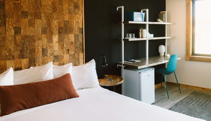 King room at the Adrift Hotel in Long Beach, Washington, with a cork accent headboard wall, work desk, and mini fridge by the window.