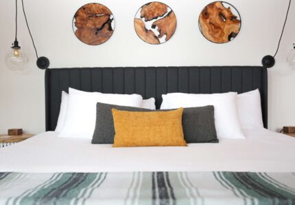 Centered view of a king bed with charcoal channel-tufted headboard, glass pendant lights, and round live-edge wood art at the Inn at Manzanita, Oregon.
