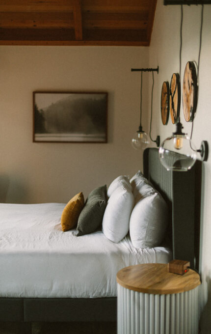 Guest room at the Inn at Manzanita, Oregon, with exposed wood beam ceilings, pendant lighting, and forest photography above the bed.