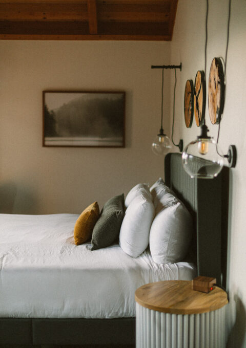 Guest room at the Inn at Manzanita, Oregon, with exposed wood beam ceilings, pendant lighting, and forest photography above the bed.