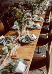 Elegant hotel dining table set with green accents, candles, and greenery, ready for guests' memorable dining experience.