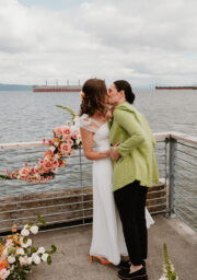 Romantic waterfront moment with floral arrangements, guests embrace, scenic views, perfect for weddings or special events.