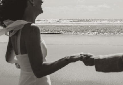Smiling couple holding hands on a serene beach with gentle waves, embodying romantic coastal getaway experience.