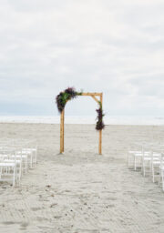 Romantic beachfront wedding setup with white chairs and floral arch under open skies by a serene ocean at luxury hotel.