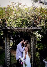 Romantic couple kissing under rustic garden pergola, lush flowers, serene atmosphere, perfect wedding venue.