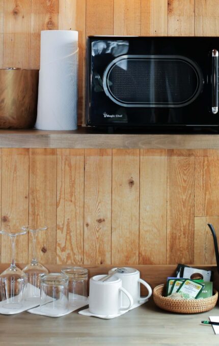 Cosy wooden kitchenette with microwave, kettle, glassware, and tea set, offering a warm welcome and convenience for guests.