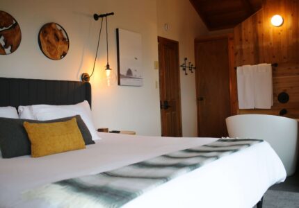 Cosy hotel room with elegant wood panelling, inviting king-sized bed, modern lighting, and a luxurious freestanding bathtub.