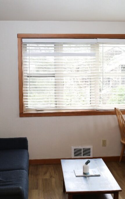 Cosy hotel room with large windows, a comfy sofa, wooden dining set, and serene views, perfect for relaxation.