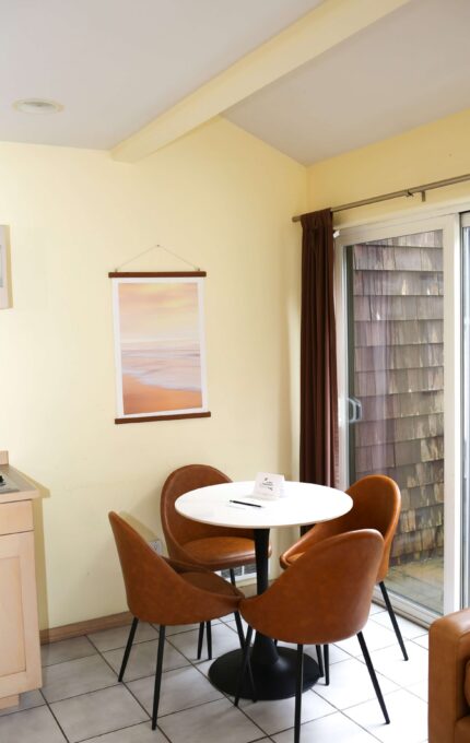 Cosy hotel room with dining table, warm lighting, sliding door to balcony; includes kitchenette and modern furniture.