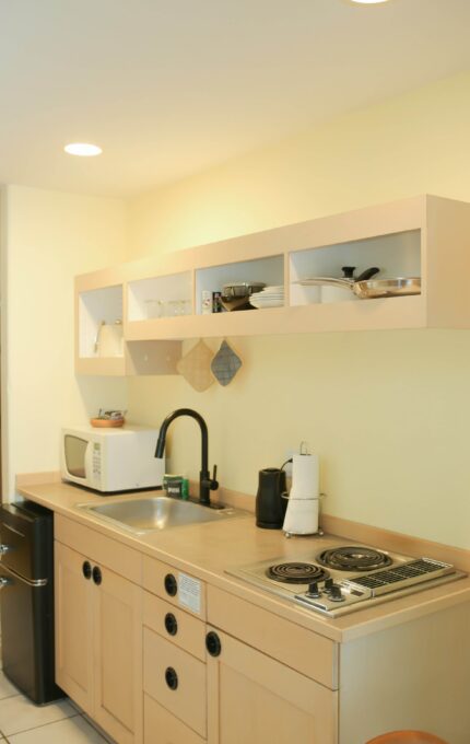 Modern hotel room kitchenette with fridge, microwave, stovetop, and open shelving for a comfortable self-catering stay.
