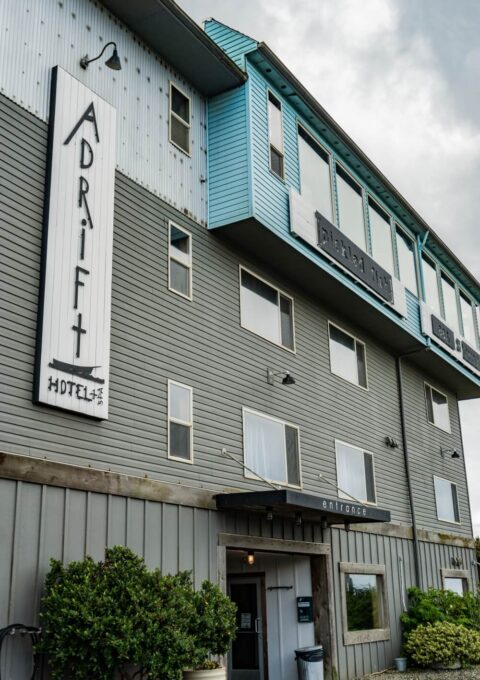 Modern coastal hotel facade with welcoming entrance, large windows, and lush greenery, perfect for a seaside getaway.