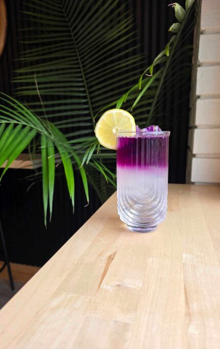 Vibrant tropical cocktail with lemon on modern wooden bar, lush greenery enhancing exotic, relaxing hotel vibe.