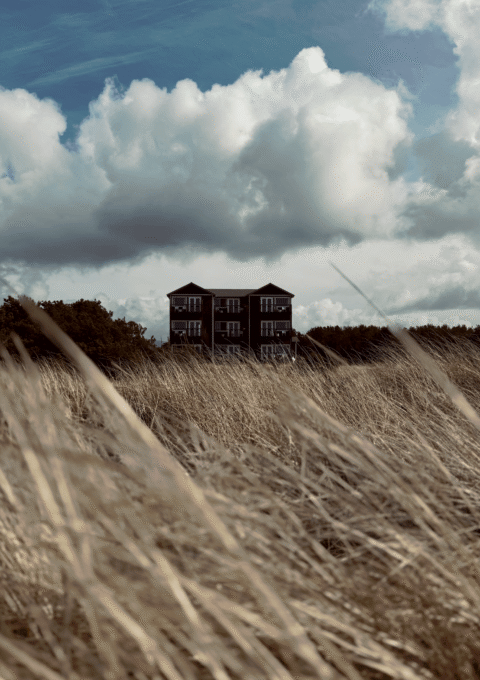Inn at Discovery Coast seen across windswept dune grass in Long Beach, Washington, under dramatic coastal clouds