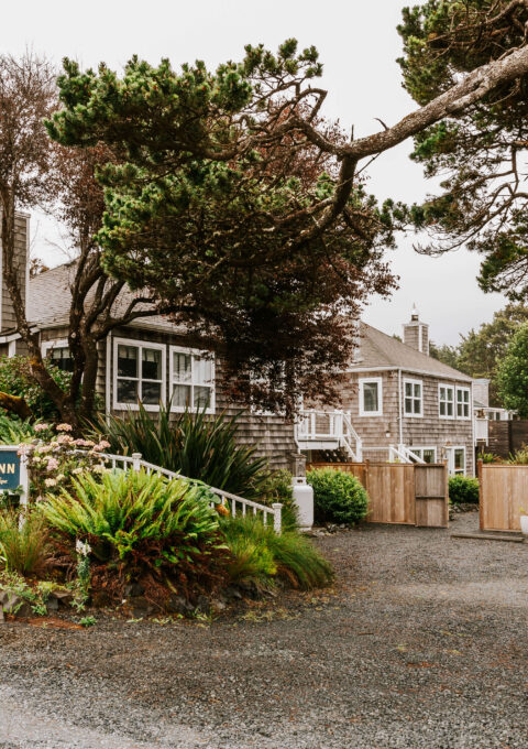 Garden entrance and 'The Inn' sign at the Inn at Arch Cape, Oregon, with lush coastal plantings along the gravel drive in Arch Cape Oregon