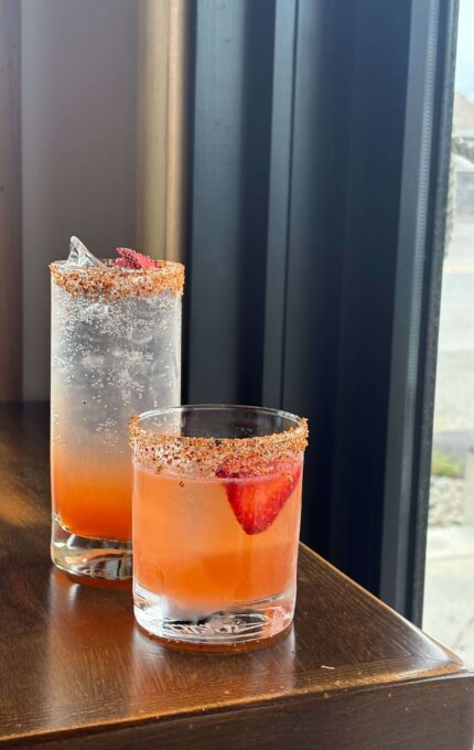 Elegant cocktails with fresh strawberries and a sprinkle of spice, set on a wooden table by a sunlit window.