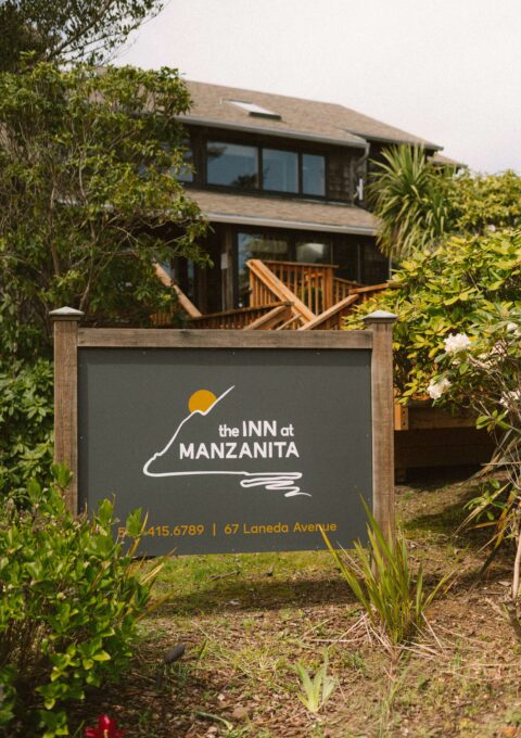 Cosy inn entrance surrounded by lush greenery, featuring rustic wooden architecture and welcoming signage.